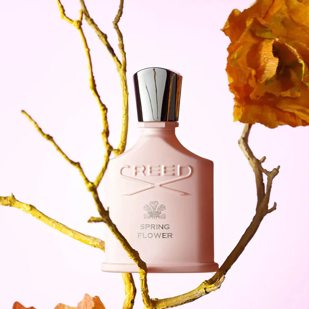 Pink Creed perfume bottle with a silver cap on a pink background with yellow flowers and branches.